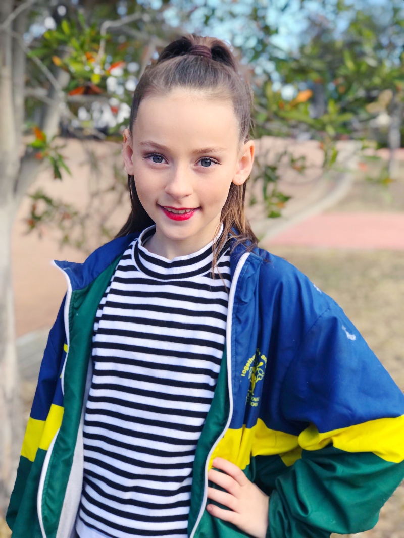 Girl with pony tail smiling in front of tree in dance clothes